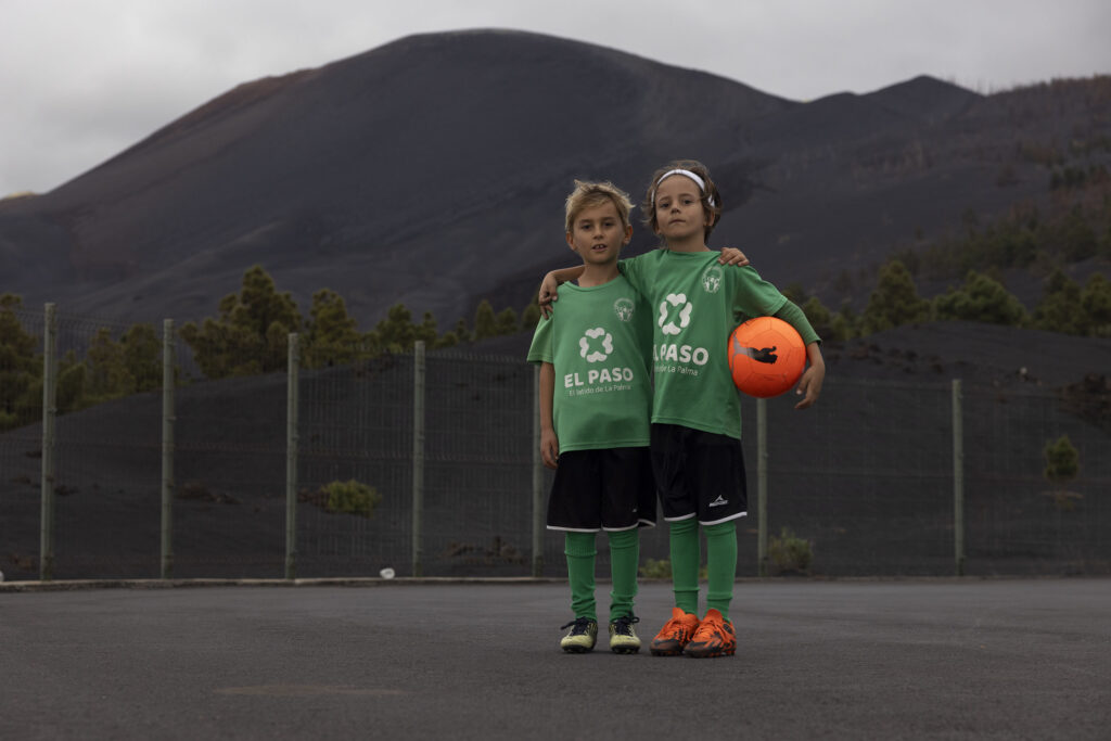 Two local children play football at a pitch below the volcano in Las Manchas. Lino (blonde hair on the left) and Ilay (with white hair band)  both aged 7.  Thier homes were not destroyed but are now separated by the lava with the road destoyed.  This football  pitch escaped the lava flows but had nearly a meter of  volcanic ash accumulate on the pitch. 

La Palma. An island of the Canaries. Two years after the Cumbre Vieja volcanic eruption in late 2021.  Photography taken on January 2024.