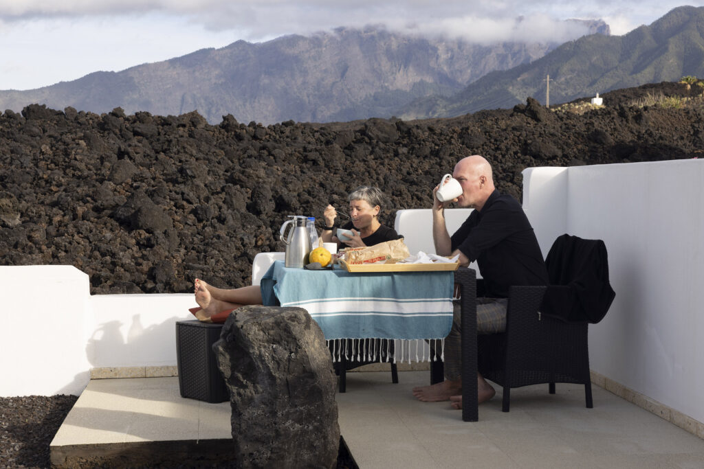 German tourists enjoy breakfast outside in the garden of their guesthouse which sits adjacent to the lava flow. 

La Palma. An island of the Canaries. Two years after the Cumbre Vieja volcanic eruption in late 2021.  Photography taken on January 2024.
